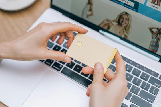 Manos sosteniendo tarjeta dorada sobre port&aacute;til con sitio web de compras.