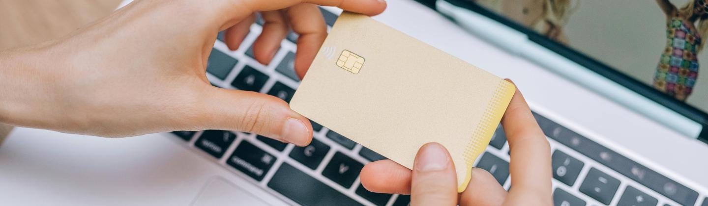 Manos sosteniendo tarjeta dorada sobre port&aacute;til con sitio web de compras.
