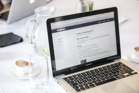 Laptop abierto en una mesa con tazas de caf&eacute; y una jarra de agua.